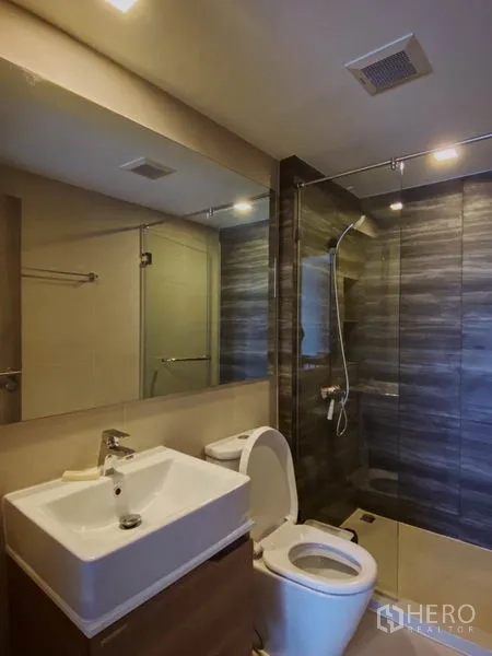 Condominium for rent in Pathum Wan, Bangkok - Contemporary bathroom with glass-enclosed shower, vanity and toilet.