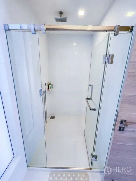 Condominium for rent or sale in Bang Rak, Bangkok - Close-up of a white walk-in shower with clear glass doors and a rain showerhead.