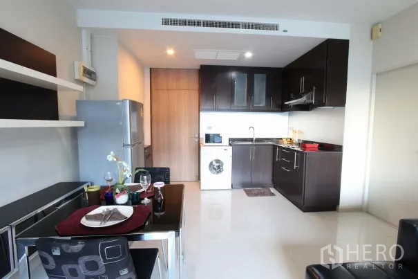 公寓 出租在Watthana, Bangkok - 开放式厨房与用餐区，深色橱柜，双门冰箱与室内洗衣机，现代泰国公寓风格。