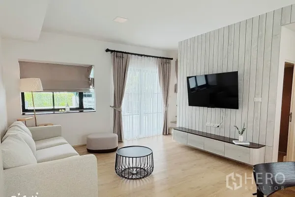 Townhouse for rent in Bang Phli, Samut Prakan - Living area with a floating TV cabinet, mounted screen, and large windows.