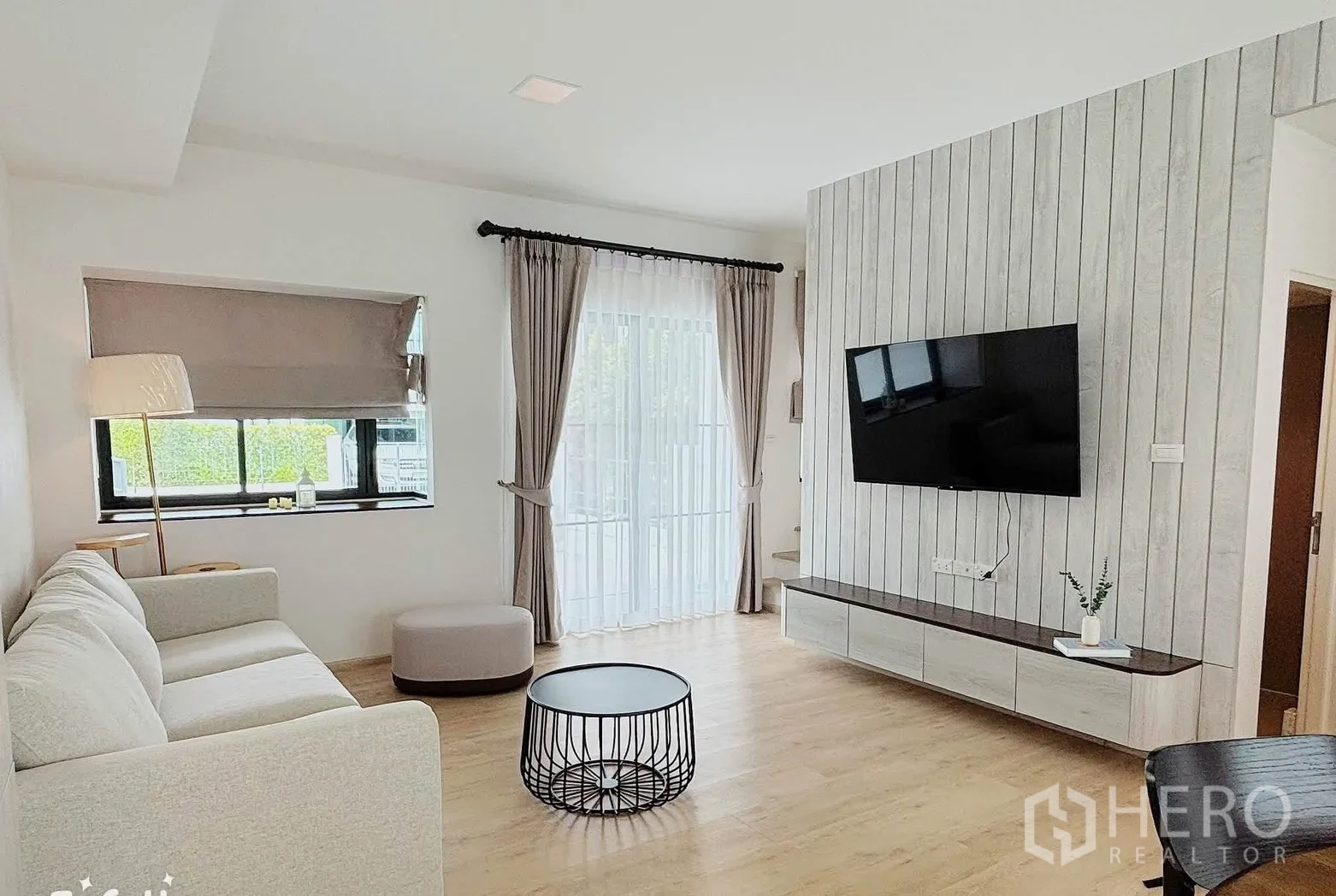 Townhouse for rent in Bang Phli, Samut Prakan - Living area with a floating TV cabinet, mounted screen, and large windows.