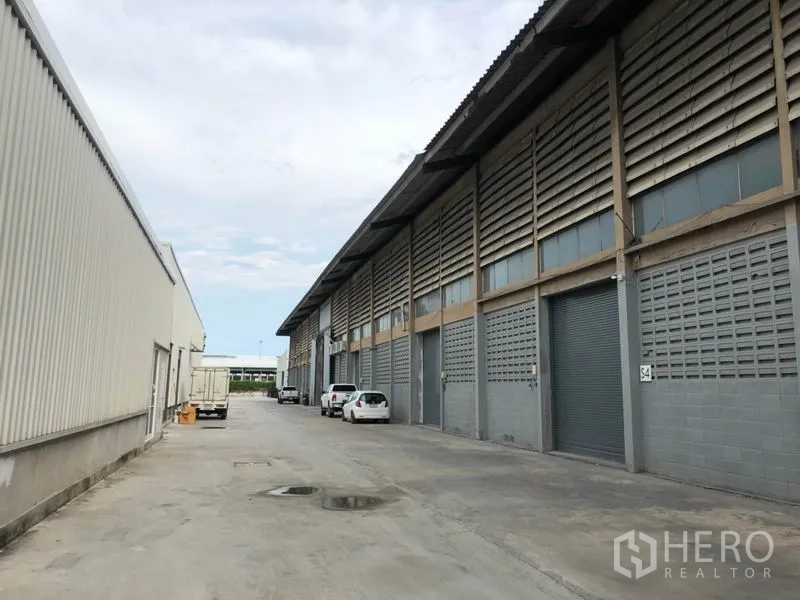 Factory for rent in Mueang Samut Prakan, Samut Prakan - Row of industrial units with roller shutter doors and a wide driveway for truck access.