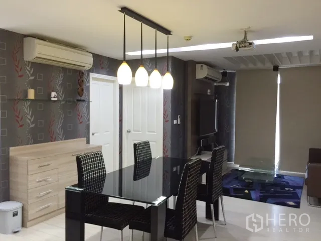 Condominium for rent or sale in Khlong Toei, Bangkok - Open-plan living and dining area with pendant lights, black glass table, wall-mounted TV and air-conditioning.