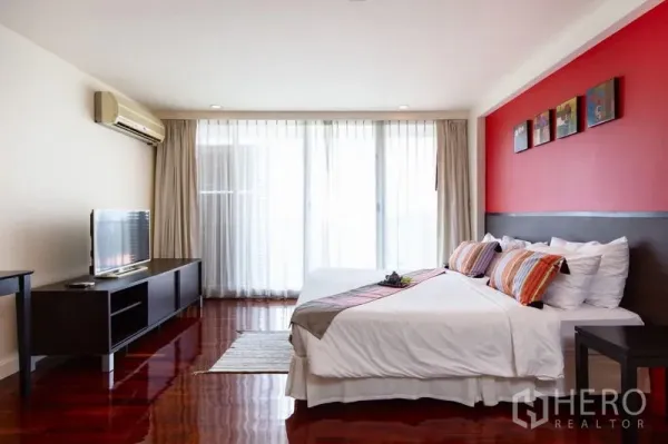 Condominium for rent in Bang Rak, Bangkok - Spacious bedroom with red accent wall, king bed, TV console and sheer curtains.