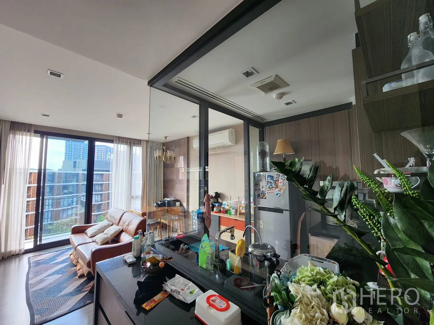 公寓 for rent in Watthana, Bangkok - 采光充足的客厅，落地窗、真皮沙发，与木饰面独立厨房以玻璃推拉门相连。