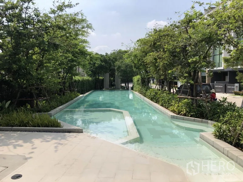 Townhouse for rent in Suan Luang, Bangkok - Long landscaped communal swimming pool shaded by trees within the project.