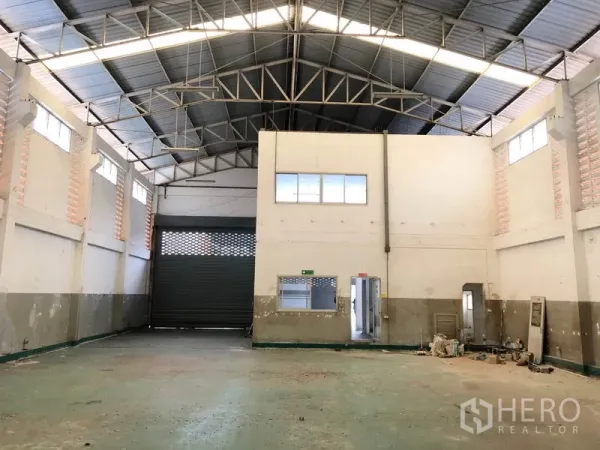 Factory for rent in Pathum Thani - High-ceiling warehouse hall with steel truss roof, internal office block and a large roller shutter door.