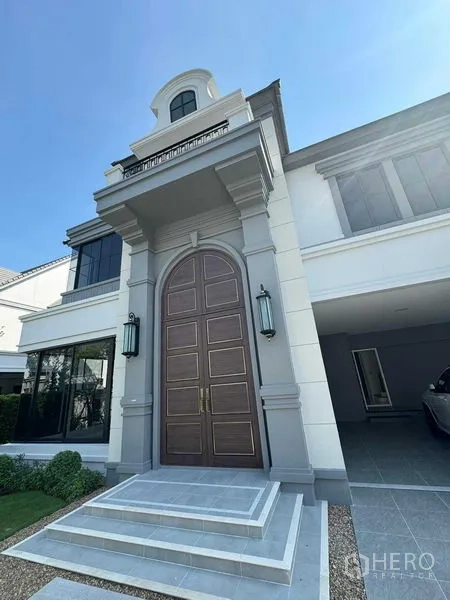 Detached House for rent in Bang Khen, Bangkok - Grand front entrance featuring an arched double wooden door, classical columns, wall lanterns and tiled steps.