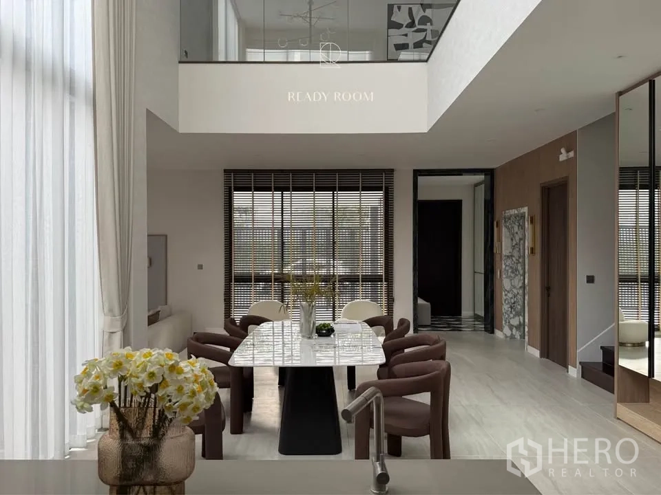 Detached House for rent in Bang Kapi, Bangkok - Dining area with marble table beneath a mezzanine with glass railing.
