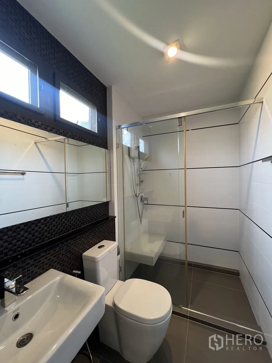 Townhouse for rent in Lat Phrao, Bangkok - Bathroom with frameless glass shower, white vanity and dark accent tiles.