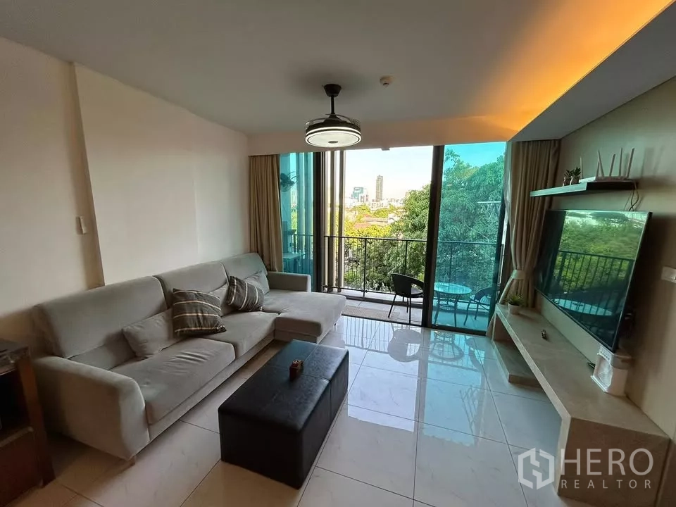 公寓 出租在Watthana, Bangkok - 采光充足的客厅通往阳台，眺望树梢与城市景