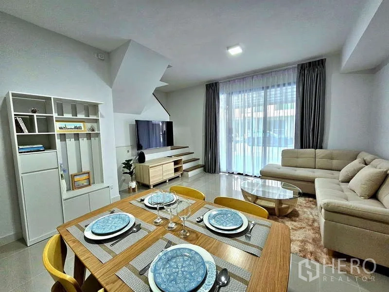 Townhouse for rent in Bang Phli, Samut Prakan - Open‑plan living and dining area with sofa, TV wall and set dining table.