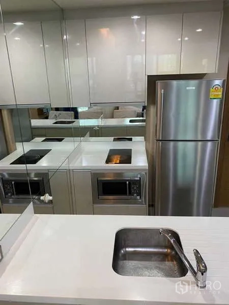 Condominium for rent in Bang Rak, Bangkok - Compact kitchen with glossy cabinets, electric hob, microwave and fridge.