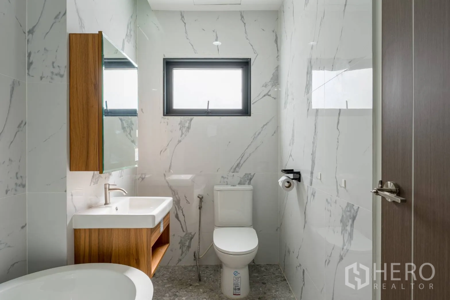 Home Office for rent in Khlong Toei, Bangkok - Compact bathroom with window, wall-mounted vanity and marble-look tiles.