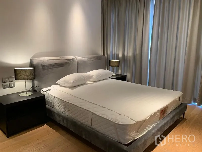 Condominium for rent in Khlong Toei, Bangkok - Spacious master bedroom featuring gray upholstered bed, twin nightstands, and blackout curtains.