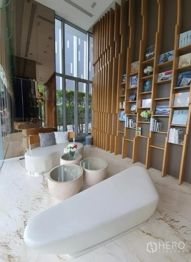 公寓 出租在Watthana, Bangkok - 阅读休息区，通顶书架与现代座椅，临近整面玻璃墙。
