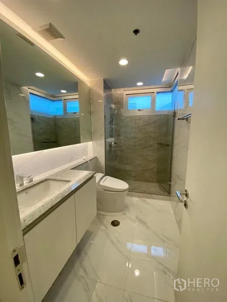 Condominium for rent in Khlong Luang, Pathum Thani - Second bathroom with glass-enclosed rain shower, white vanity and polished tile floor.