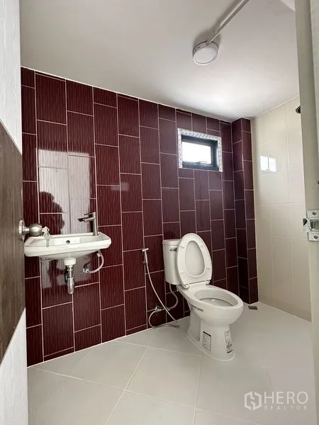 Factory for rent or sale in Sai Noi, Nonthaburi - Clean restroom with white sanitary ware and maroon accent wall tiles.