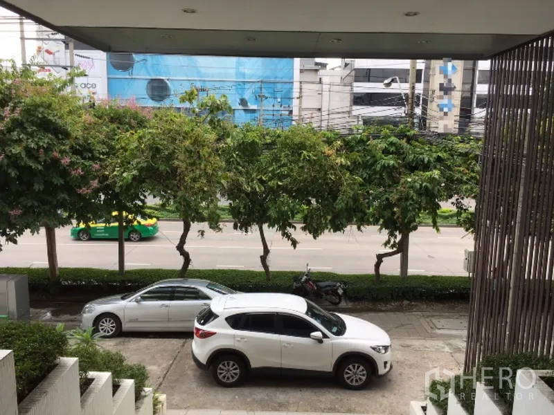 สำนักงานที่บ้าน ให้เช่าในHuai Khwang, Bangkok - ลานจอดรถหน้าตึก มีรถยนต์ ต้นไม้ และทางเท้าริมถนนใหญ่.