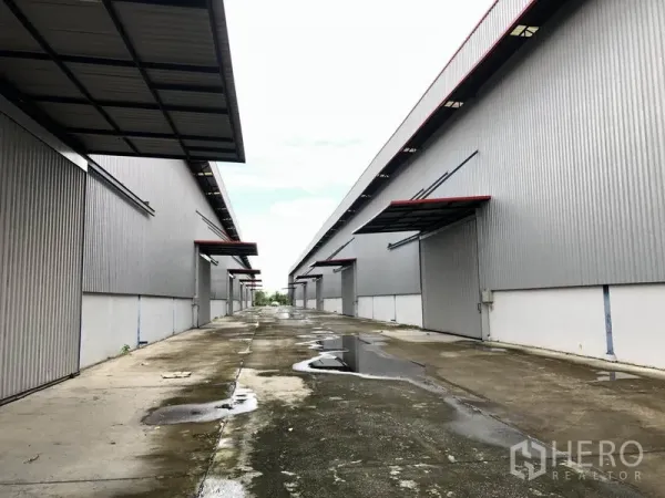 Factory for rent or sale in Phra Nakhon Si Ayutthaya - Service lane after rain with several loading docks on both sides of the warehouses.