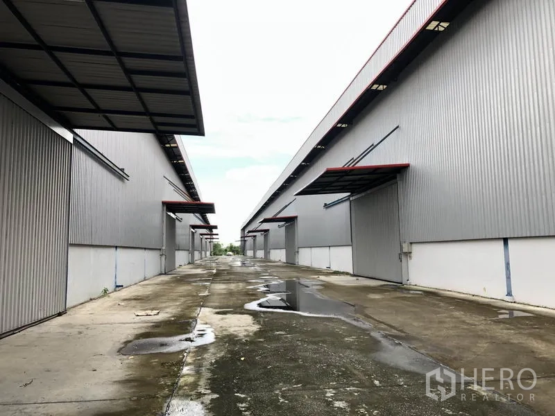 Factory for rent or sale in Phra Nakhon Si Ayutthaya - Service lane after rain with several loading docks on both sides of the warehouses.