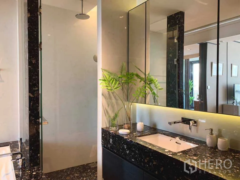 Condominium for rent in Khlong Toei, Bangkok - Contemporary bathroom with marble vanity, backlit mirror and glass-enclosed rain shower.