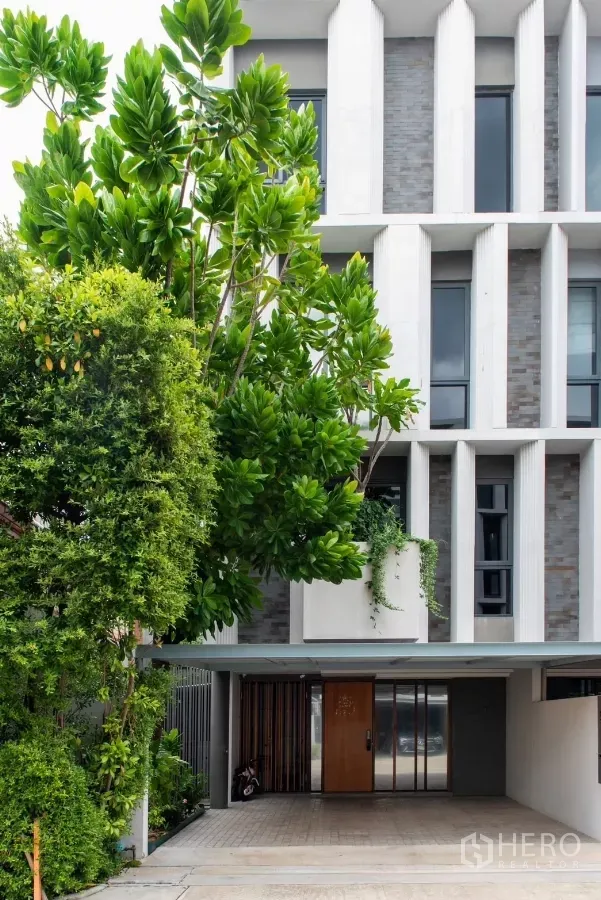 Townhouse for rent in Lat Phrao, Bangkok - Contemporary townhouse facade with covered parking and lush greenery.