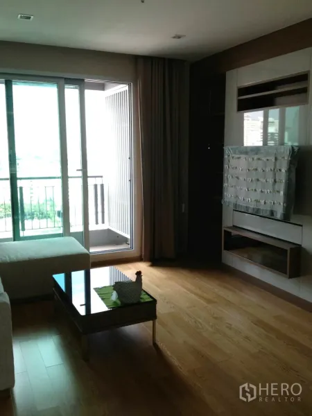 公寓 出租在Ratchathewi, Bangkok - 明亮客厅，木地板，推拉落地玻璃门通向阳台，沙发与电视柜一体化。