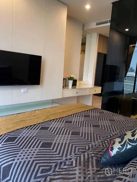 Condominium for sale in Pathum Wan, Bangkok - Bedroom with mounted TV, work vanity and patterned bedding.