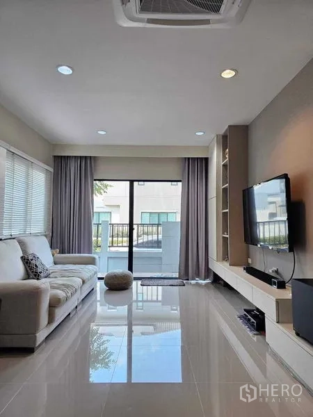 Detached House for sale in Khan Na Yao, Bangkok - Sunny living room with sofa, built-in TV wall and sliding doors to the balcony.