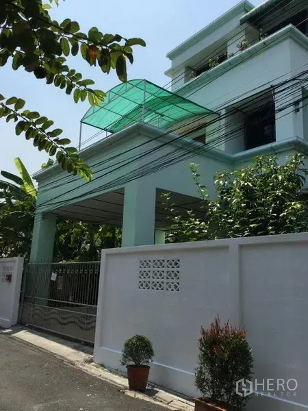 Detached House for rent or sale in Huai Khwang, Bangkok - Exterior of a multi-storey mint-green detached house with gated carport and rooftop canopy.