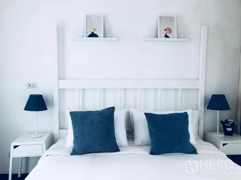 Townhouse for rent in Khlong Toei, Bangkok - Minimal white bedroom with double bed, blue cushions and bedside lamps.