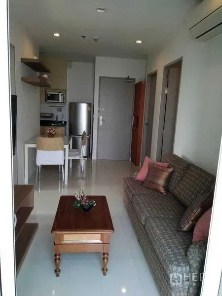 公寓 出租在Watthana, Bangkok - 开放式客厅，配沙发、电视柜、餐桌与精巧小厨房。