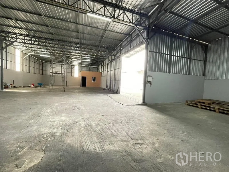 Warehouse for rent in Nakhon Pathom - Open storage floor with large entry, metal wall panels, and stacked pallets inside the warehouse.