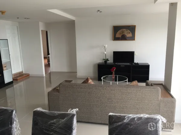 Condominium for rent in Khlong Toei, Bangkok - Lounge with a gray sofa, TV console, glass coffee table and glossy tiled floors.