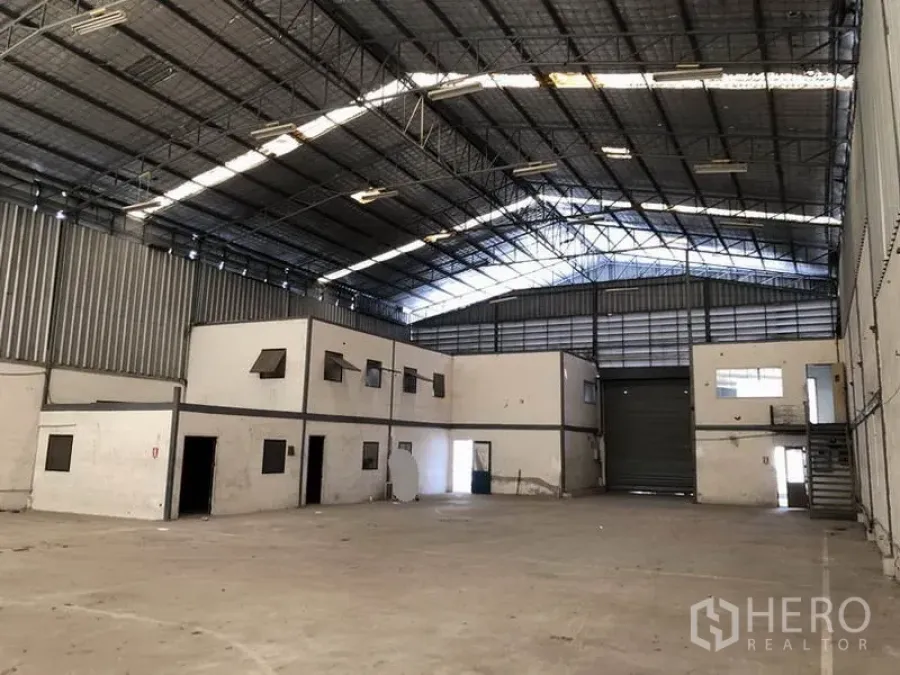 Warehouse for rent in Suan Luang, Bangkok - Large warehouse interior with high steel truss roof, mezzanine offices and a wide roller shutter.