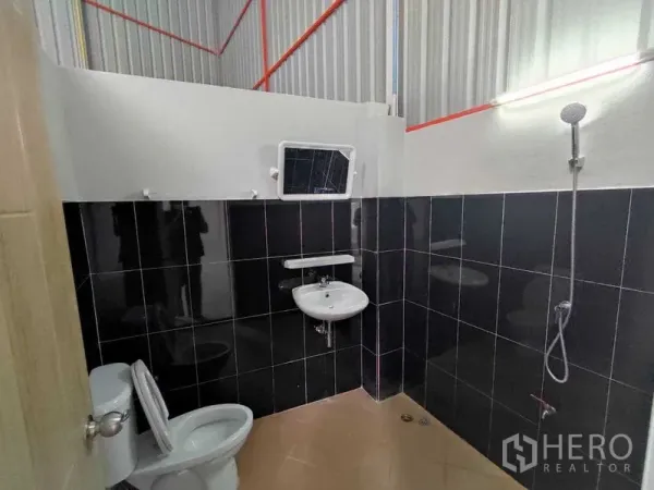 货栈 出租在Pak Kret, Nonthaburi - 仓库卫生间，带坐便器、挂墙洗手盆和淋浴，黑色瓷砖墙面。