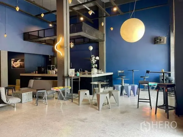 店屋 出租在Lat Phrao, Bangkok - 一层挑高蓝色空间，吊灯点缀，吧台与多样座位。