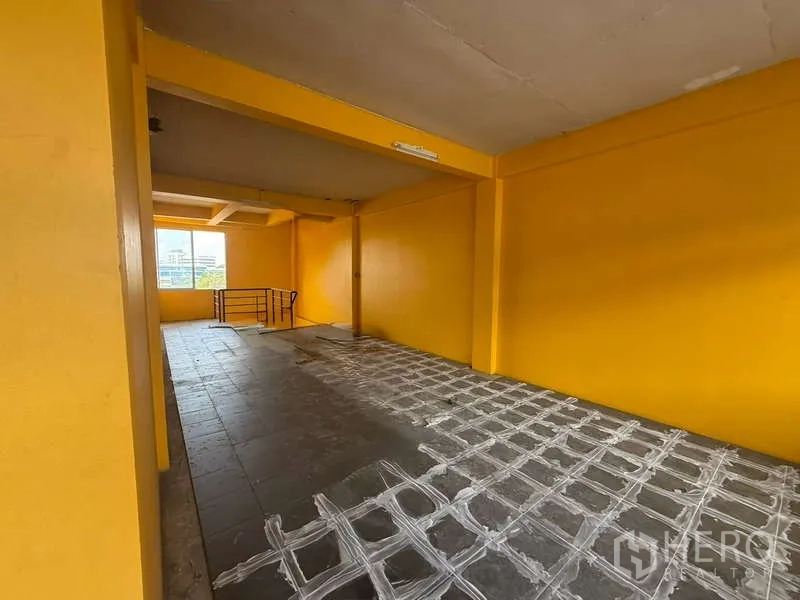 Home Office for rent in Khlong Toei, Bangkok - Long hall-like section with window and railing, yellow walls and grey flooring.