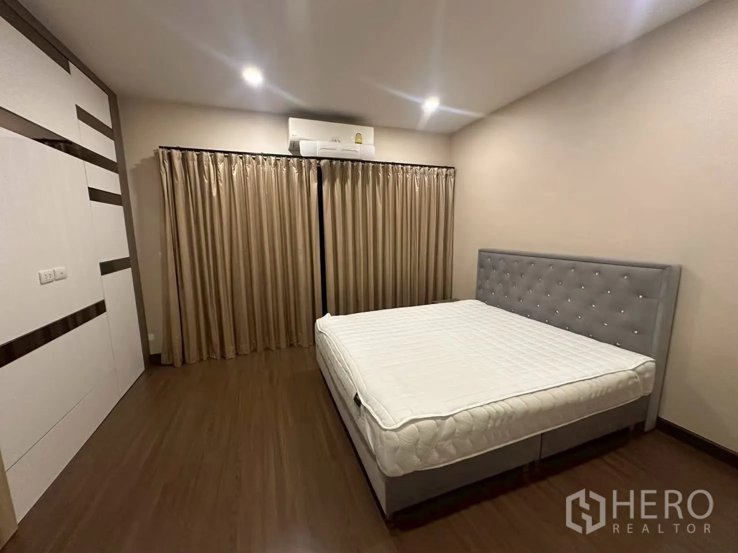 Detached House for rent in Bang Phli, Samut Prakan - Large bedroom with grey headboard, full curtains and a wall air conditioner.