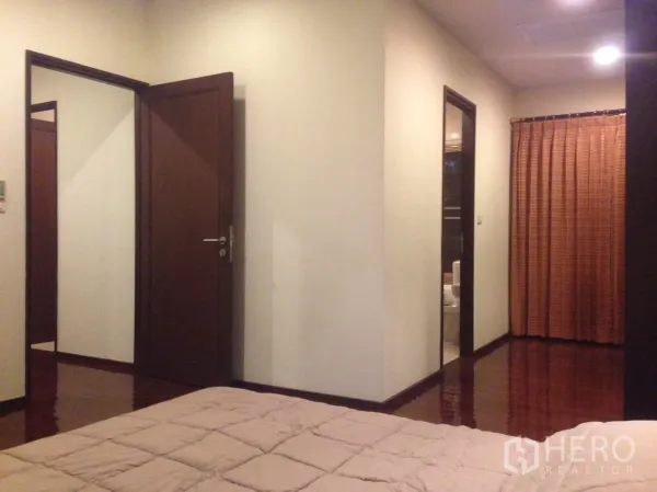 公寓 出租在Watthana, Bangkok - 主卧朝走廊与套内卫生间的视角，暖色灯光与落地窗帘。