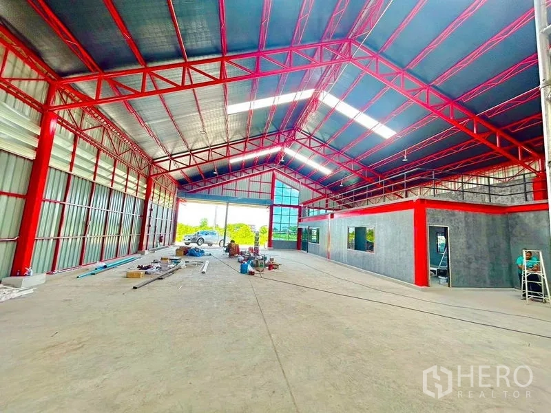 Warehouse for rent in Lam Luk Ka, Pathum Thani - Spacious high-ceiling warehouse interior with red steel trusses, concrete floor and an office block.