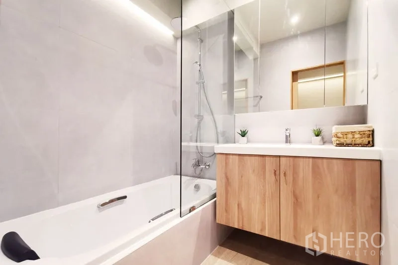 Townhouse for rent in Khlong Toei, Bangkok - Modern bathroom with bathtub, glass shower screen and wood vanity with mirror storage.