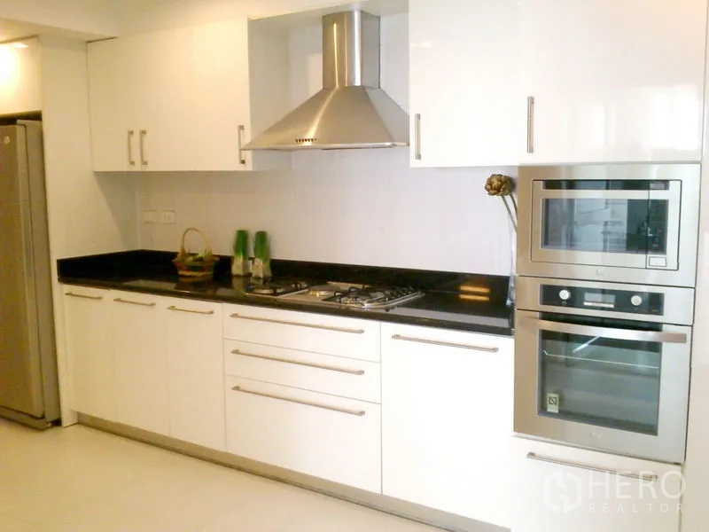 Condominium for rent in Khlong Toei, Bangkok - Modern white kitchen with gas hob, range hood, built-in oven and microwave.