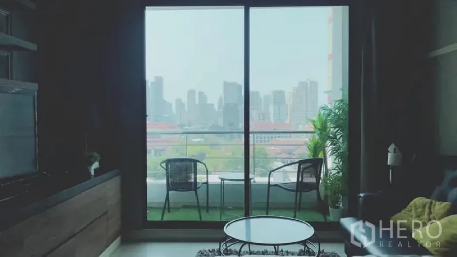 Condominium for rent in Watthana, Bangkok - Living room opening to a balcony with two chairs and a Bangkok skyline city view.