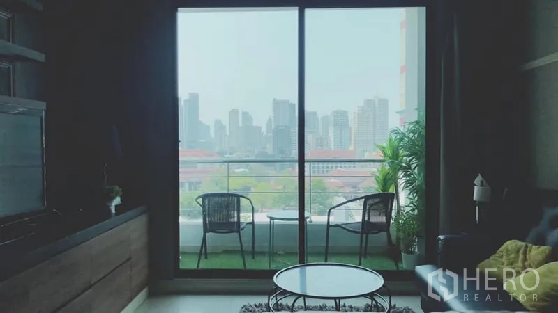 Condominium for rent in Watthana, Bangkok - Living room opening to a balcony with two chairs and a Bangkok skyline city view.