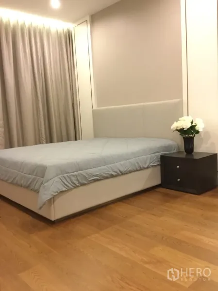 Condominium for rent in Sathon, Bangkok - Cozy bedroom with upholstered headboard, bedside table, full curtains and warm wood flooring.