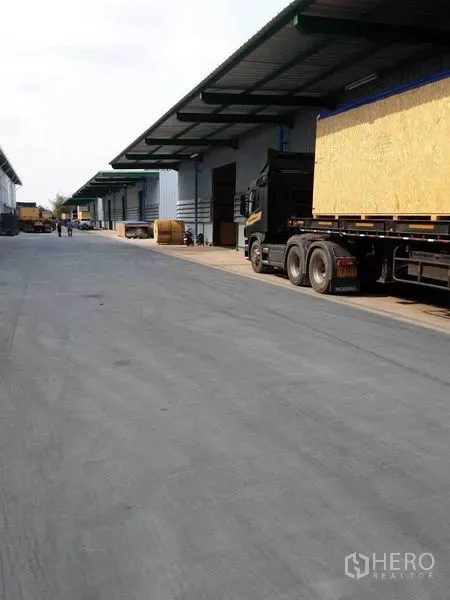 Warehouse for rent in Prawet, Bangkok - Wide driveway with trucks loading at sheltered docks in an industrial warehouse complex.