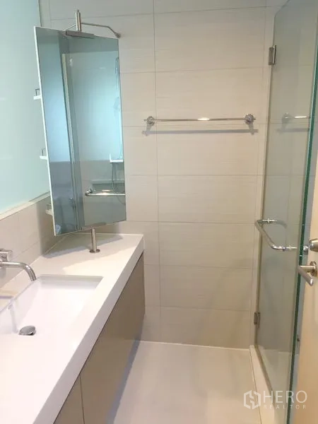 Condominium for rent in Khlong Toei, Bangkok - Modern bathroom featuring a long vanity, mirror cabinet and a glass-enclosed shower.
