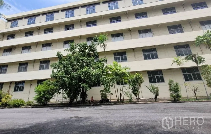 Factory for rent in Mueang Samut Prakan, Samut Prakan - Facade of multi-storey industrial building with trees and driveway